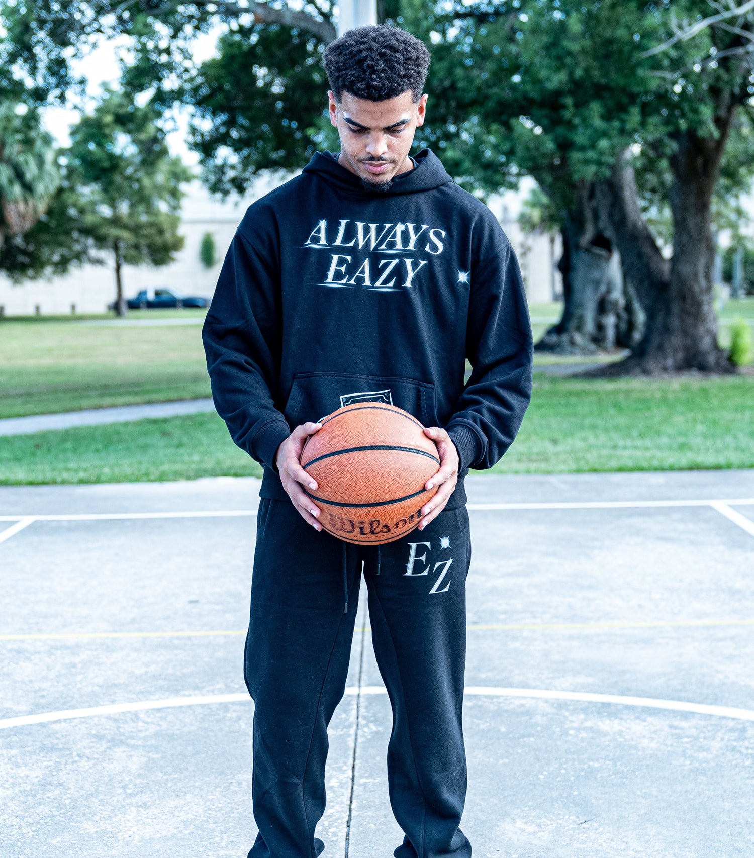 Person holding a basketball on a court wearing an 'Always Eazy' two piece set